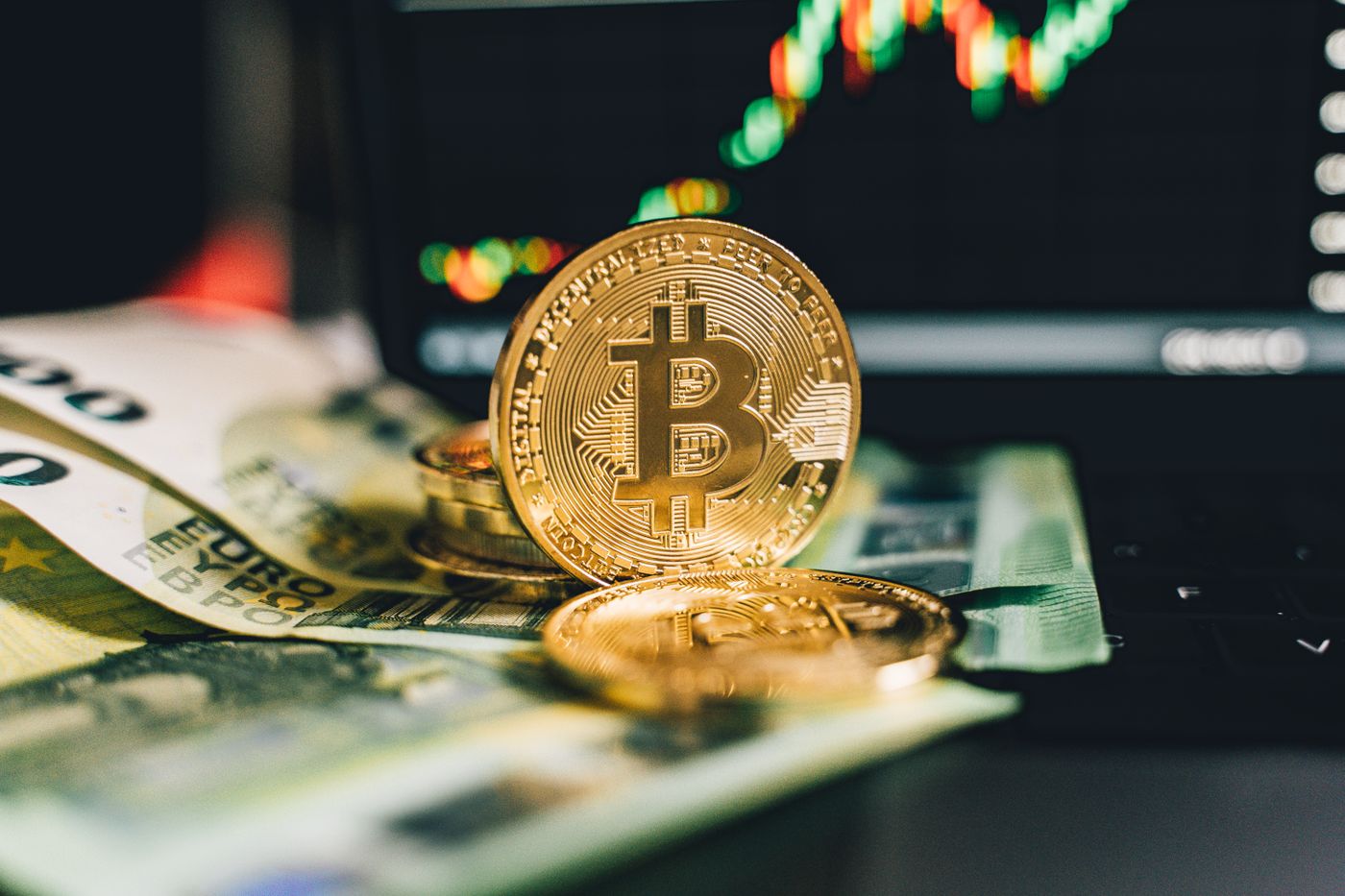 Close-up of Bitcoin and Euro notes on laptop keyboard with market chart in background.