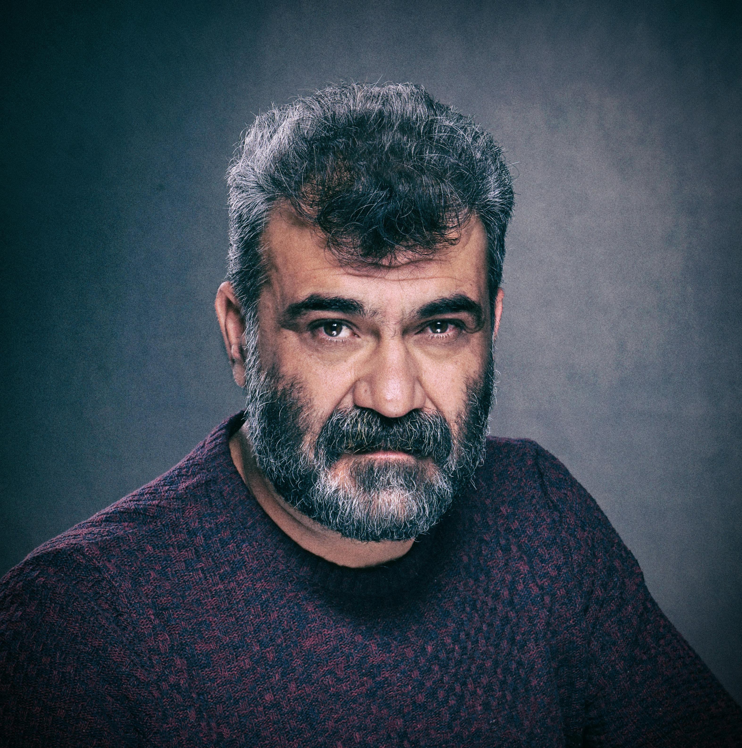 A striking portrait of a middle-aged man with a beard against a gray background.