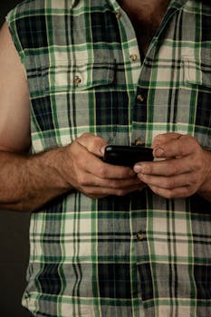 Close-up image of a man in a plaid shirt using a smartphone indoors.