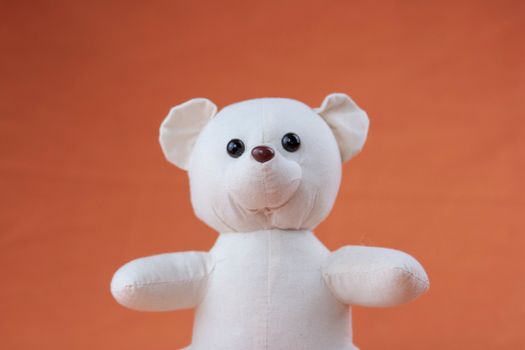 Cute stuffed teddy bear against an orange background, perfect for child-related themes.