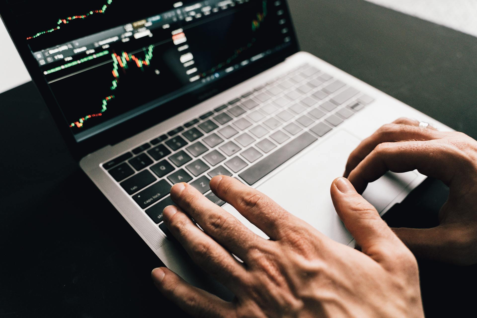 Close-up of hands typing on a laptop with stock market graphs, ideal for finance or business themes.