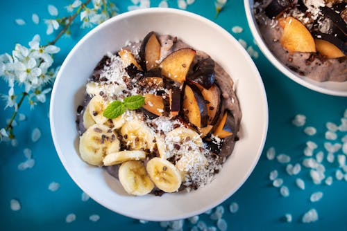 Top view of appetizing smoothie bowl topped with fresh sliced bananas and plums and decorated with coconut flakes