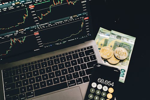 Bitcoins and Paper Money Beside a Cellphone and Laptop with Graphs on Screen 
