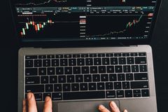 Close-up of hands using a laptop displaying stock market charts.