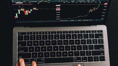 Close-up of hands using a laptop displaying stock market charts.