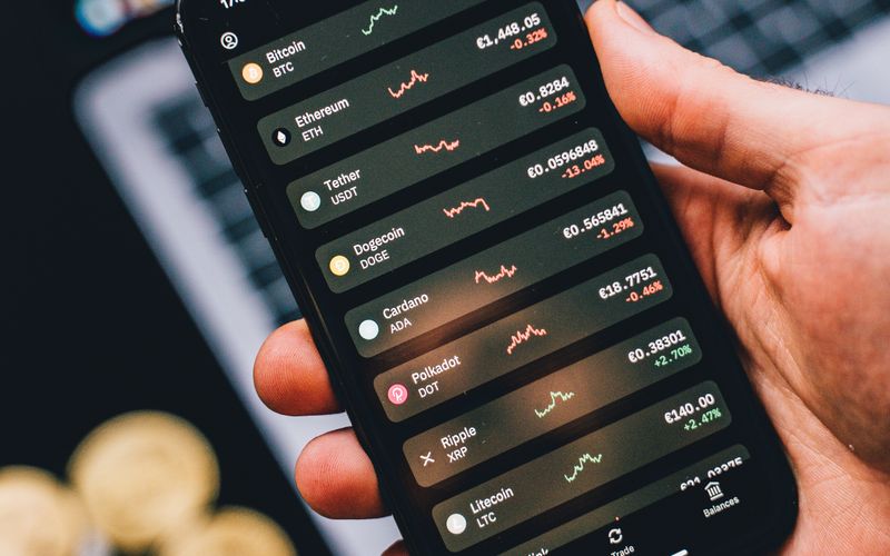 Person holding a smartphone displaying cryptocurrency trends with coins in the background