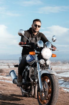 Man in sunglasses riding a motorcycle in a stunning outdoor setting under a blue sky.