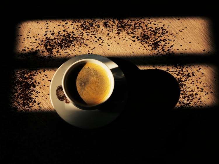 A Cup Of Coffee On A Wooden Surface With Scattered Coffee Granules