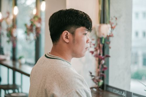 Free A young man wearing a gray sweater gazes thoughtfully out a window in an indoor setting. Stock Photo