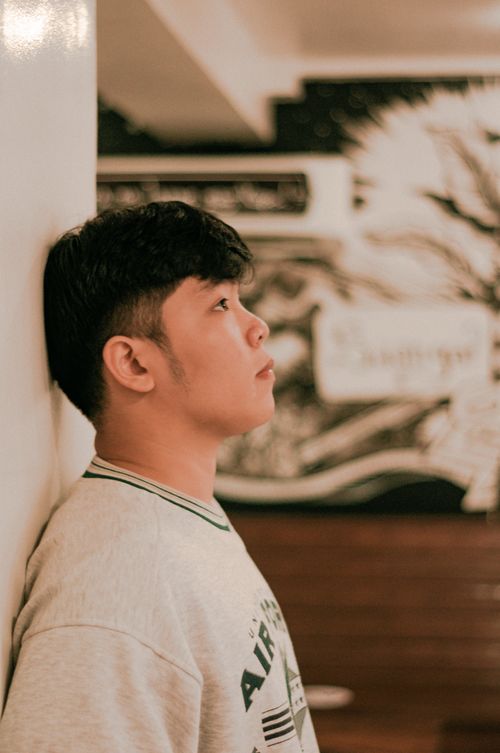 Free Profile of a young man in a gray shirt leaning against a wall indoors. Stock Photo