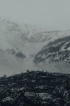 Captivating winter mountain scene with snow and fog creating a dramatic atmosphere.