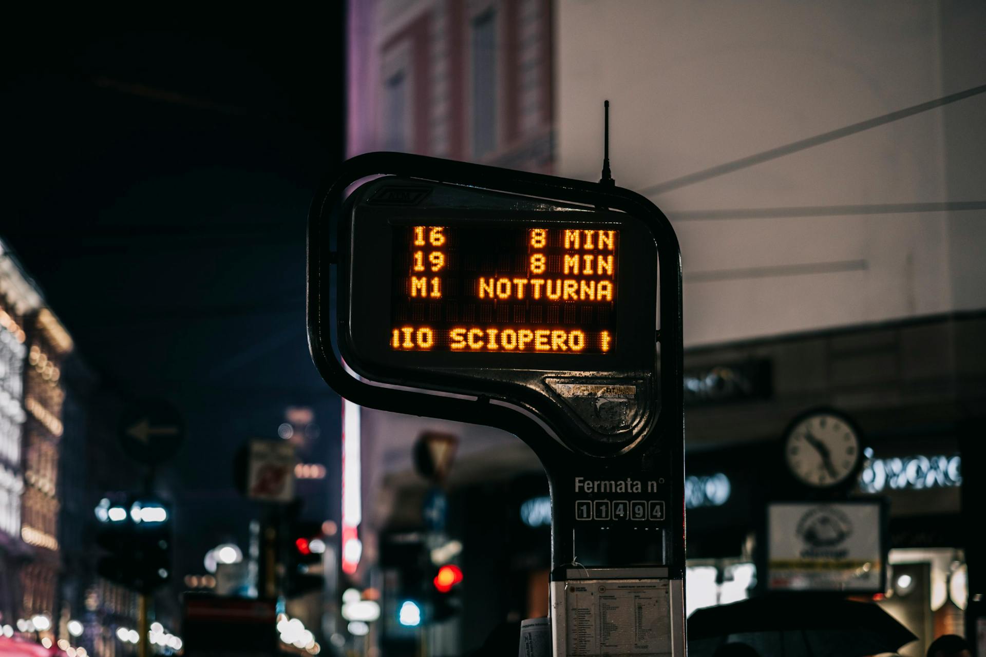 A night view of an Italian bus stop featuring illuminated signage and city lights.