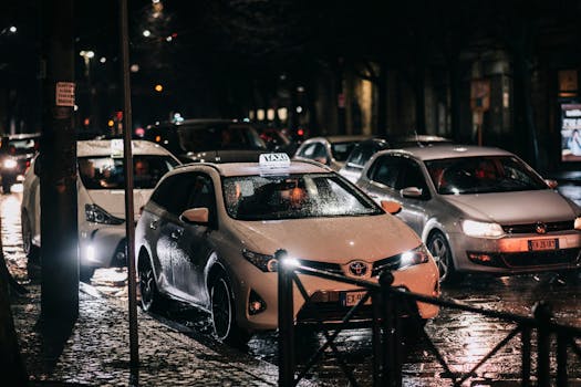 Busy city street at night with cars and taxis on a wet road, reflecting lights.