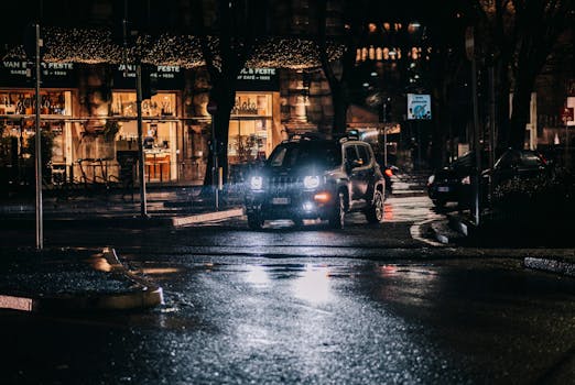 A rainy night city street scene with cars and bright storefronts, capturing reflections and moody lighting.
