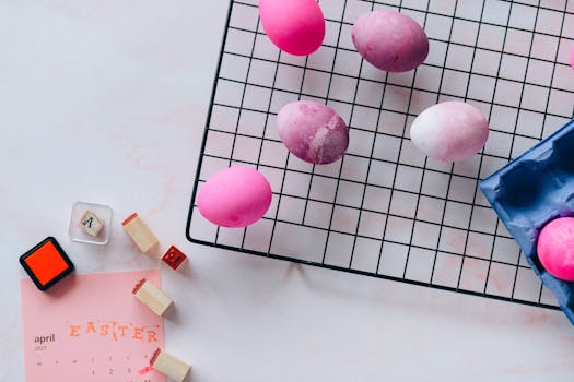 Flat lay of vibrant painted Easter eggs on drying rack with April calendar and stamp blocks.
