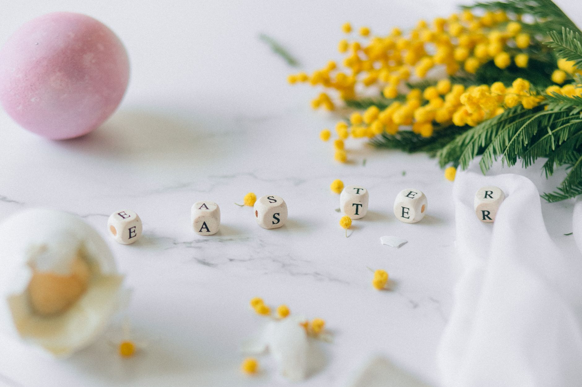 Aesthetic Easter-themed arrangement with letters, eggshells, and yellow flowers on a marble surface.