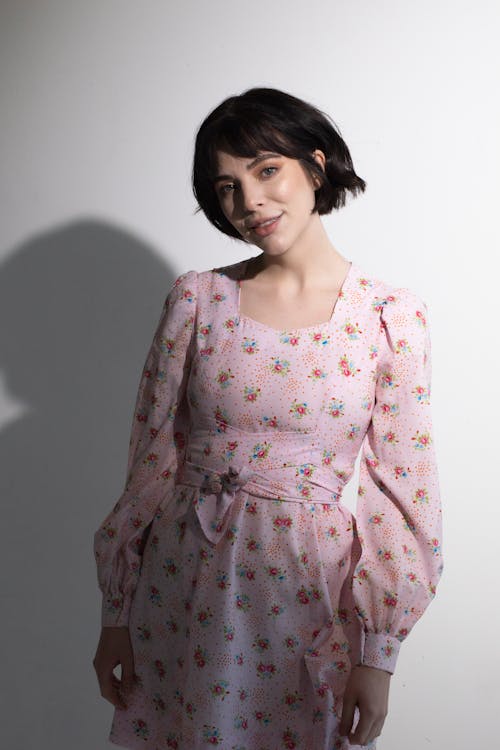 Trendy woman in dress looking at camera against white wall