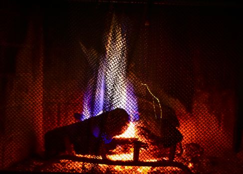 Close-up of a burning fireplace with bright flames behind a mesh screen, creating a warm ambiance.