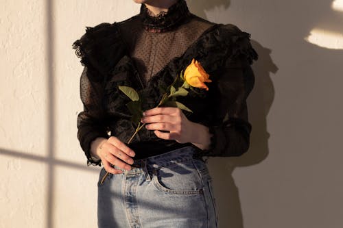 Anonymous woman with rose in hands near wall with shadows