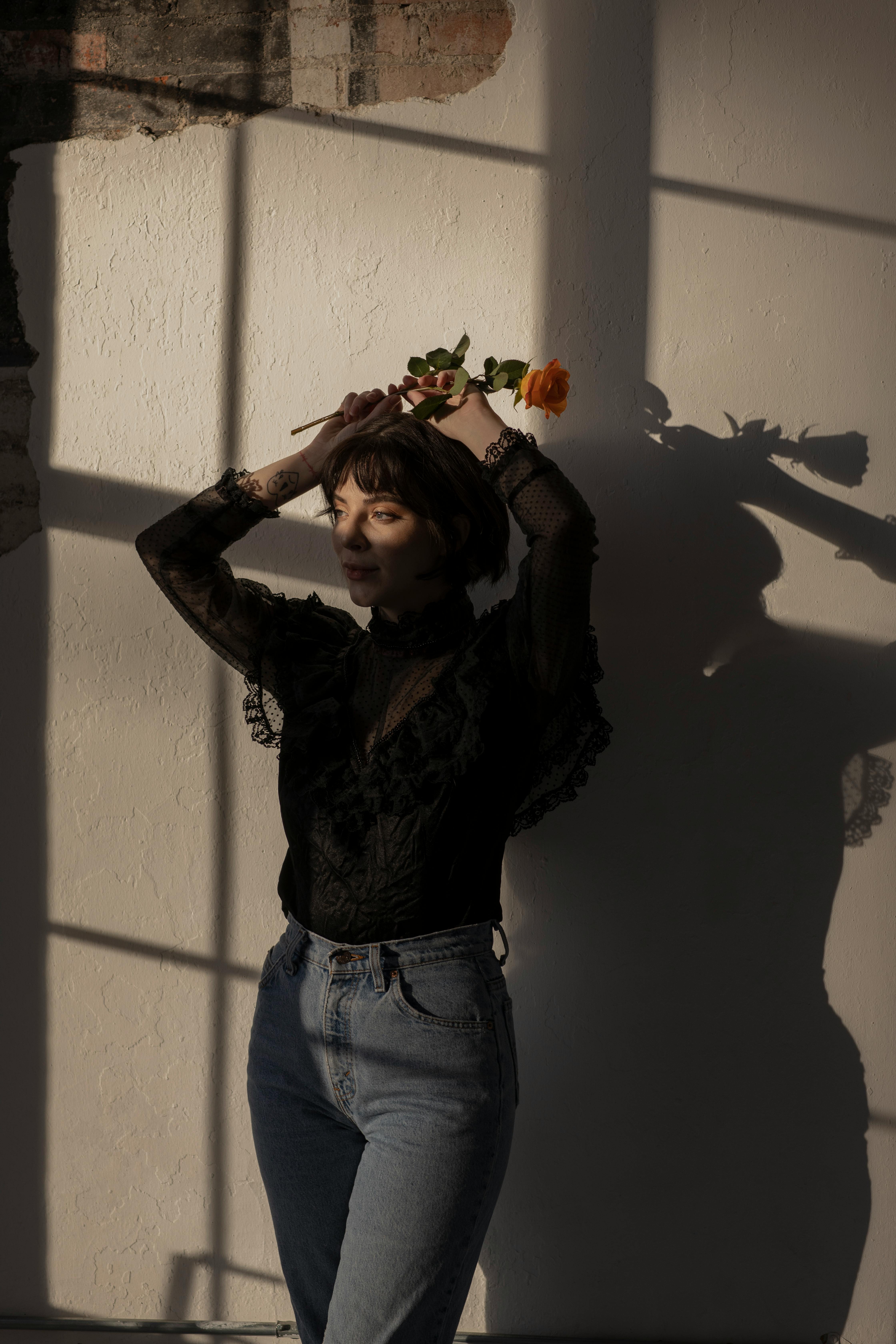 A fashionable woman poses with an orange rose, accentuated by dramatic shadows in a stylish portrait.