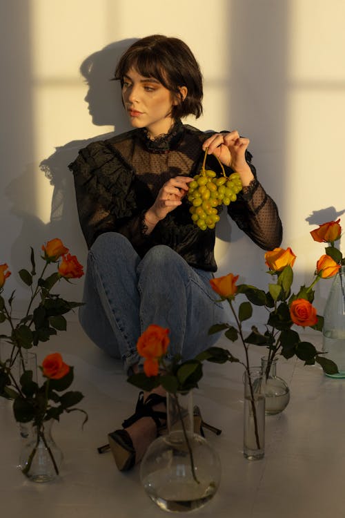 A Woman Sitting on the Floor Holding a Cluster of Grapes