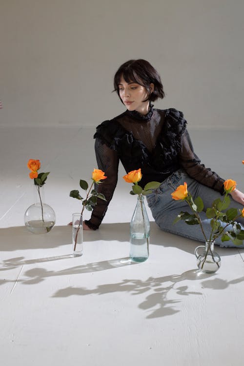 Woman Sitting in Front of Glass Vases with Orange Roses 