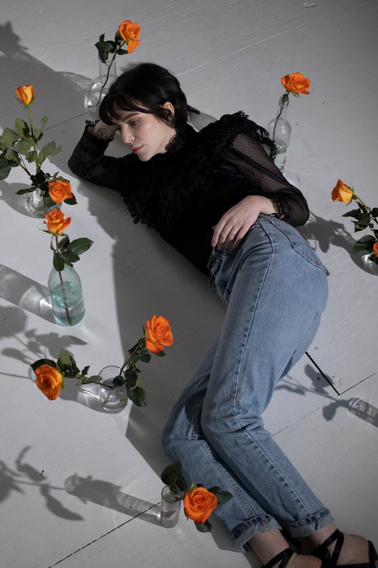 Gothic Woman In Jeans Among Roses In Blossom In Vases