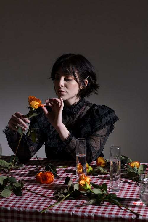 Woman in black outfit touching gentle petals of orange rose