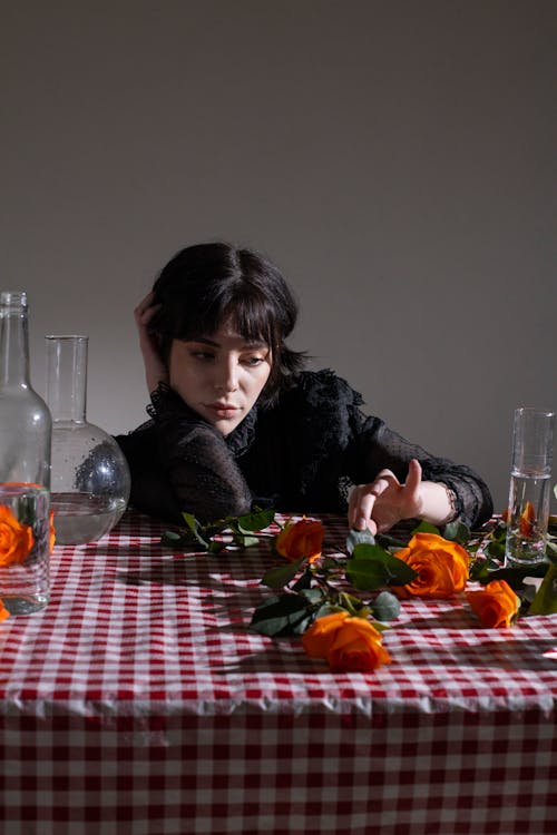 Free Dreamy young female with short dark hair at table with glassware and orange roses in blossom Stock Photo