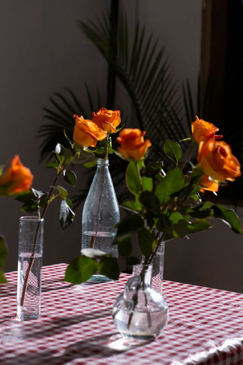 Free Bouquets of bright orange roses in blossom in glass vases with water on table at home Stock Photo