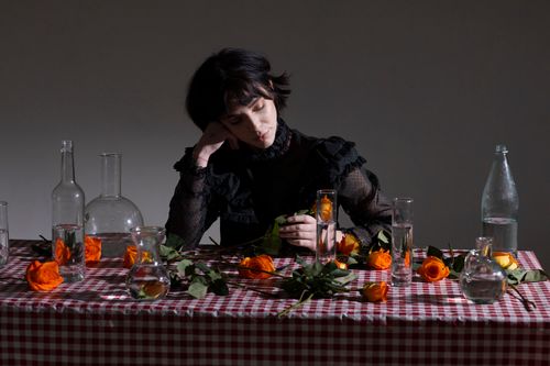 Free Thoughtful female with short dark hair at table with glassware with clean water and fresh roses with orange petals Stock Photo