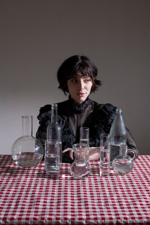Thoughtful gothic woman at table with glass flasks