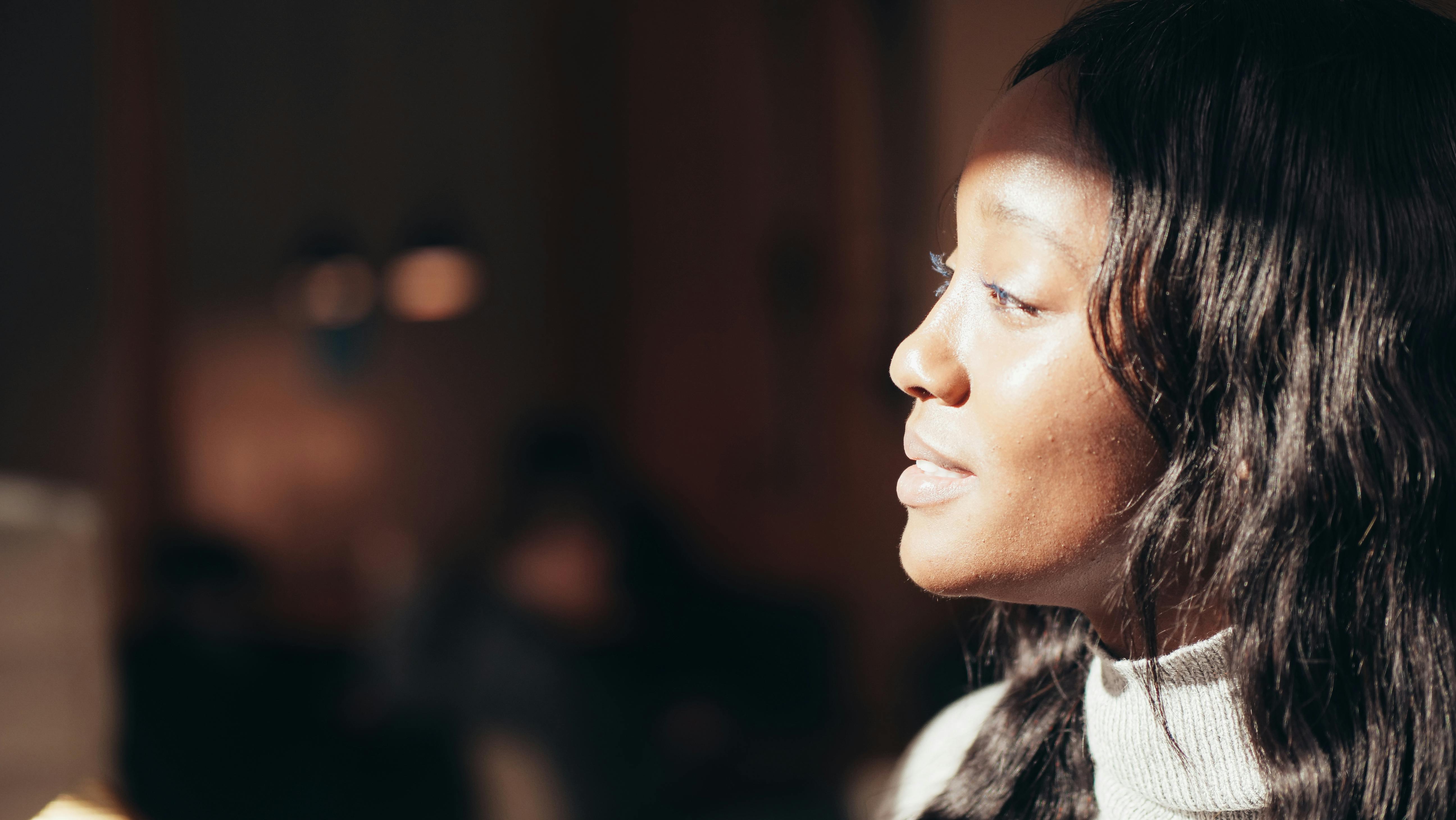A close-up, side profile portrait of a black woman with soft lighting indoors, adding warmth and tranquility.
