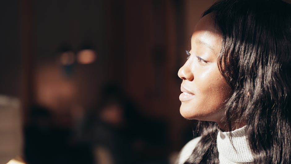 A close-up, side profile portrait of a black woman with soft lighting indoors, adding warmth and tranquility.