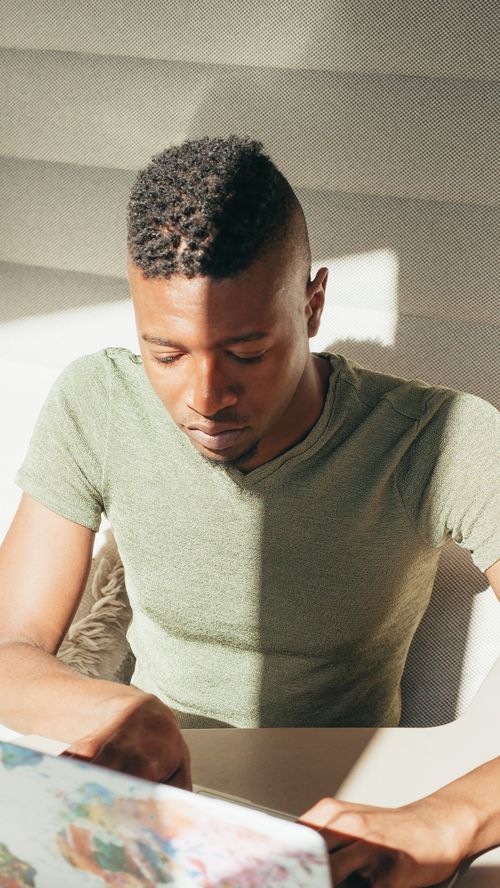 Free A young man focuses on his laptop, bathed in dramatic light and shadow in an indoor office setting. Stock Photo