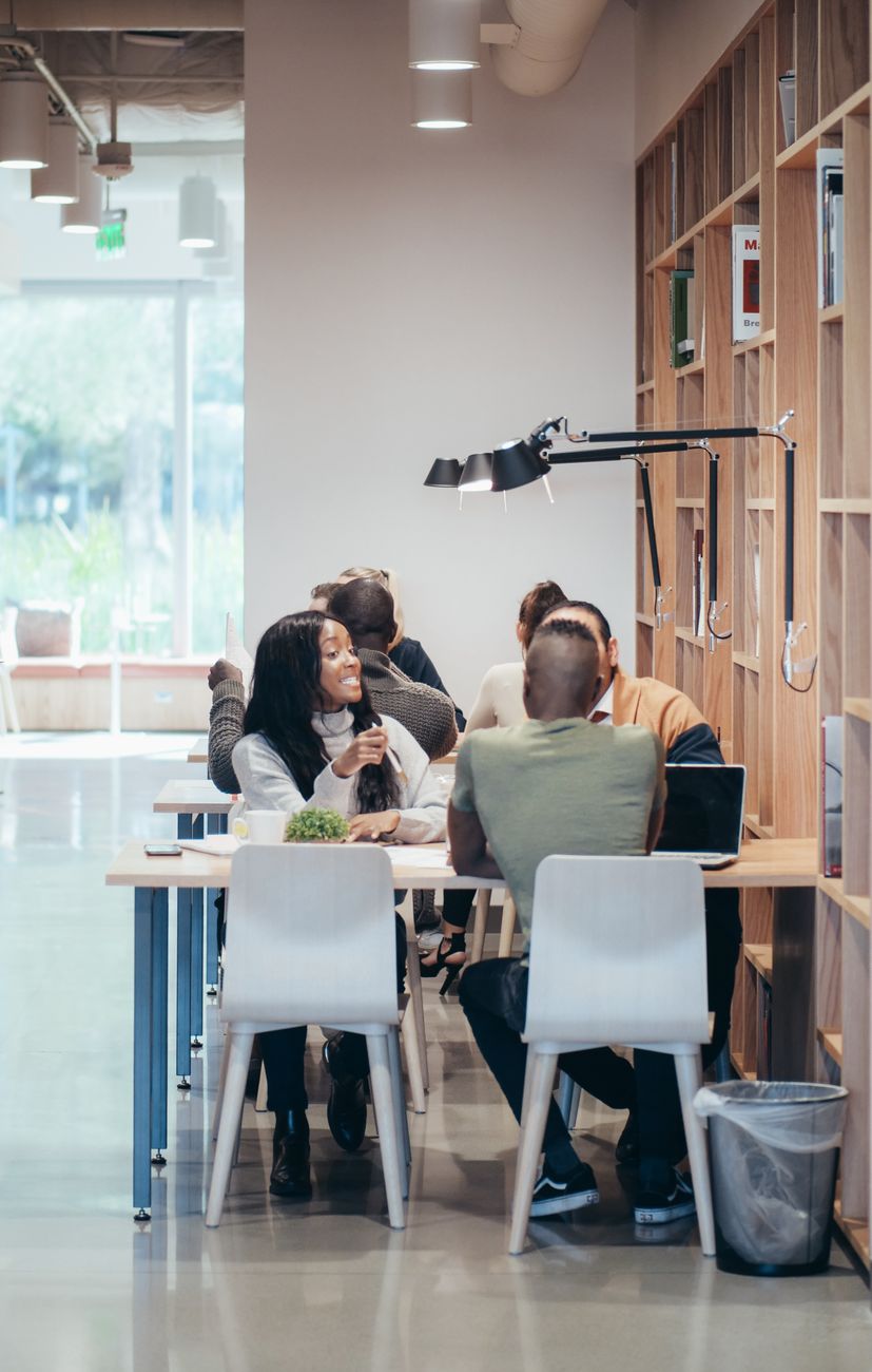 Group of adults engaged in teamwork and discussion in a bright indoor office space.