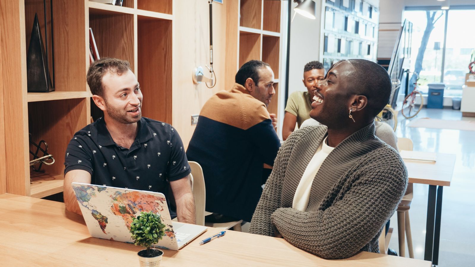 Colleagues gathered around a table in a modern coworking space discussing a laptop backpack sourcing programme.