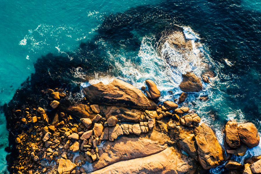A stunning aerial shot showcasing waves crashing against a rugged rocky coastline, highlighting the natural beauty of the ocean.