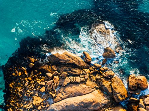 Free A stunning aerial shot showcasing waves crashing against a rugged rocky coastline, highlighting the natural beauty of the ocean. Stock Photo