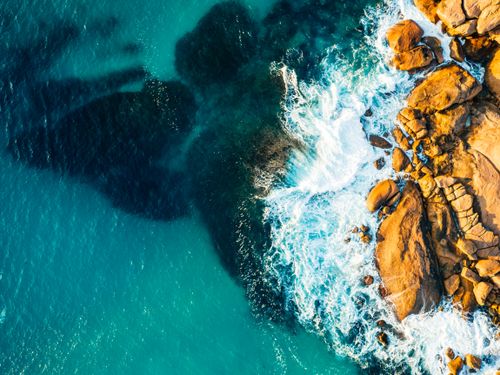 Free Drone shot captures ocean waves crashing on rugged rocks. Scenic coastal beauty. Stock Photo