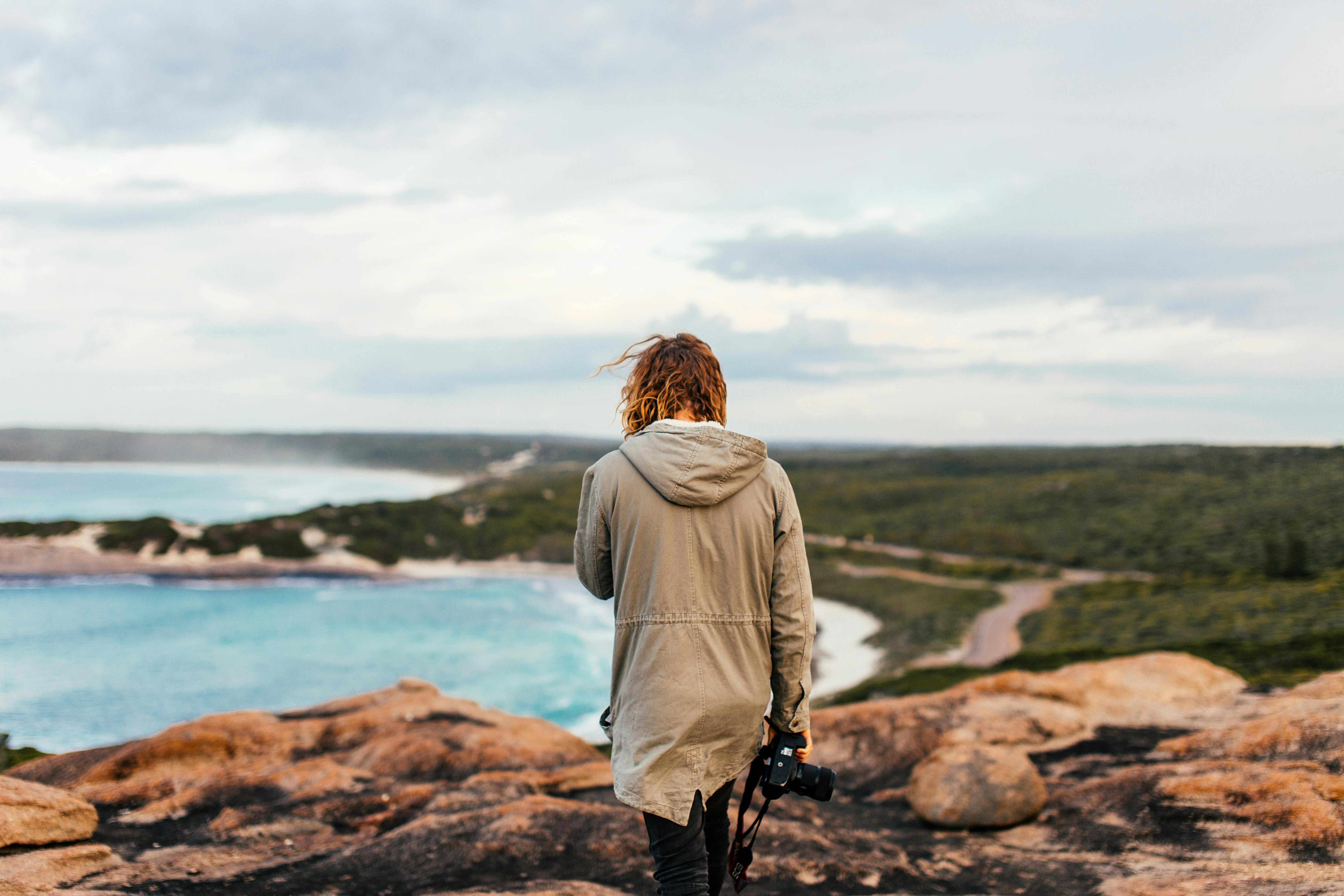 woman holding a camera and walking on a cliff