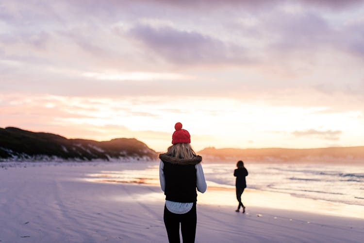 Back View Of A Woman Walking On A Beach At Sunset In Winter 