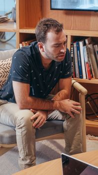 A man sits thoughtfully in a contemporary office setting with bookshelves.