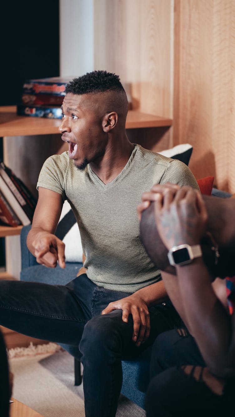 A Man Sitting On A Chair Shouting While Pointing Hid Finger