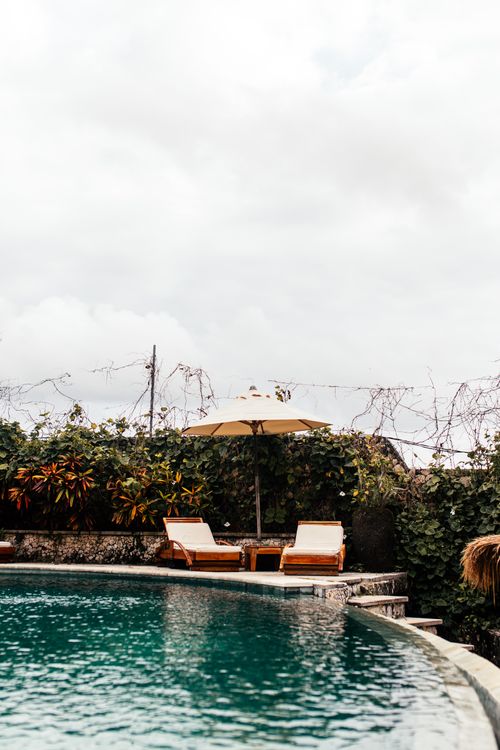 Free Peaceful poolside scene with two lounge chairs and umbrella, perfect for a relaxing getaway. Stock Photo