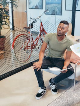 Modern office scene with a young professional holding paperwork, next to a bicycle.