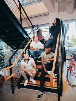 A group of diverse colleagues brainstorming together on office stairs, embracing teamwork.