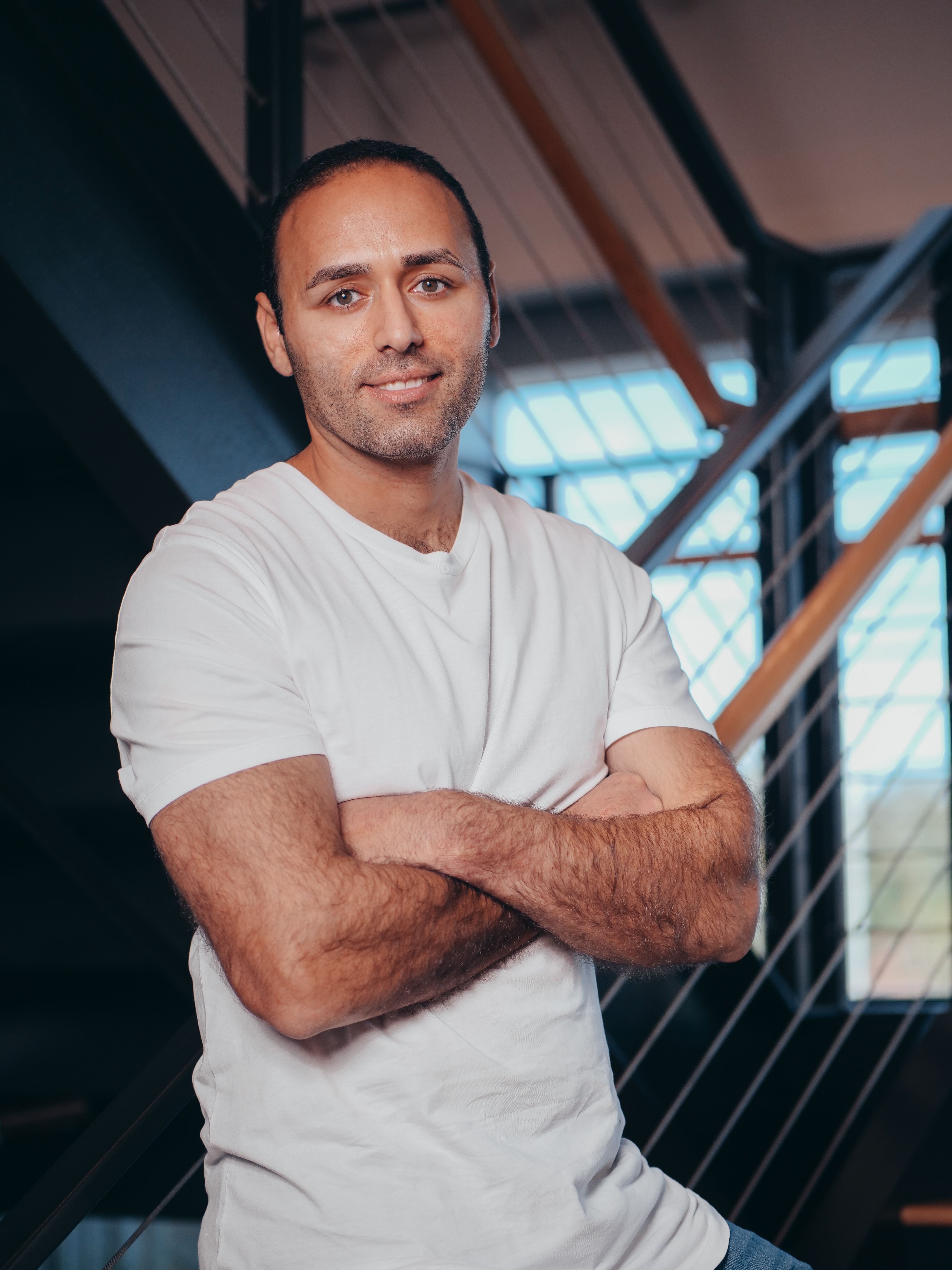 Confident man posing with arms crossed indoors by a modern staircase.