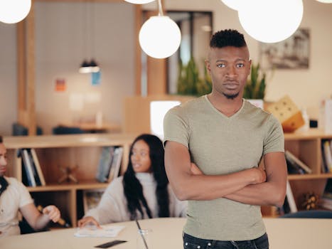 Confident man posing at a contemporary office workspace with colleagues in background.