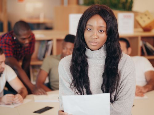 Free Portrait of a young woman holding paper amidst a group study session indoors. Stock Photo